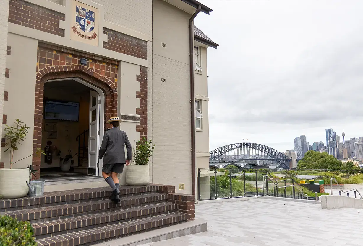 Shore student entering a heritage boarding house on campus with views of the Sydney Harbour Bridge in the background.
