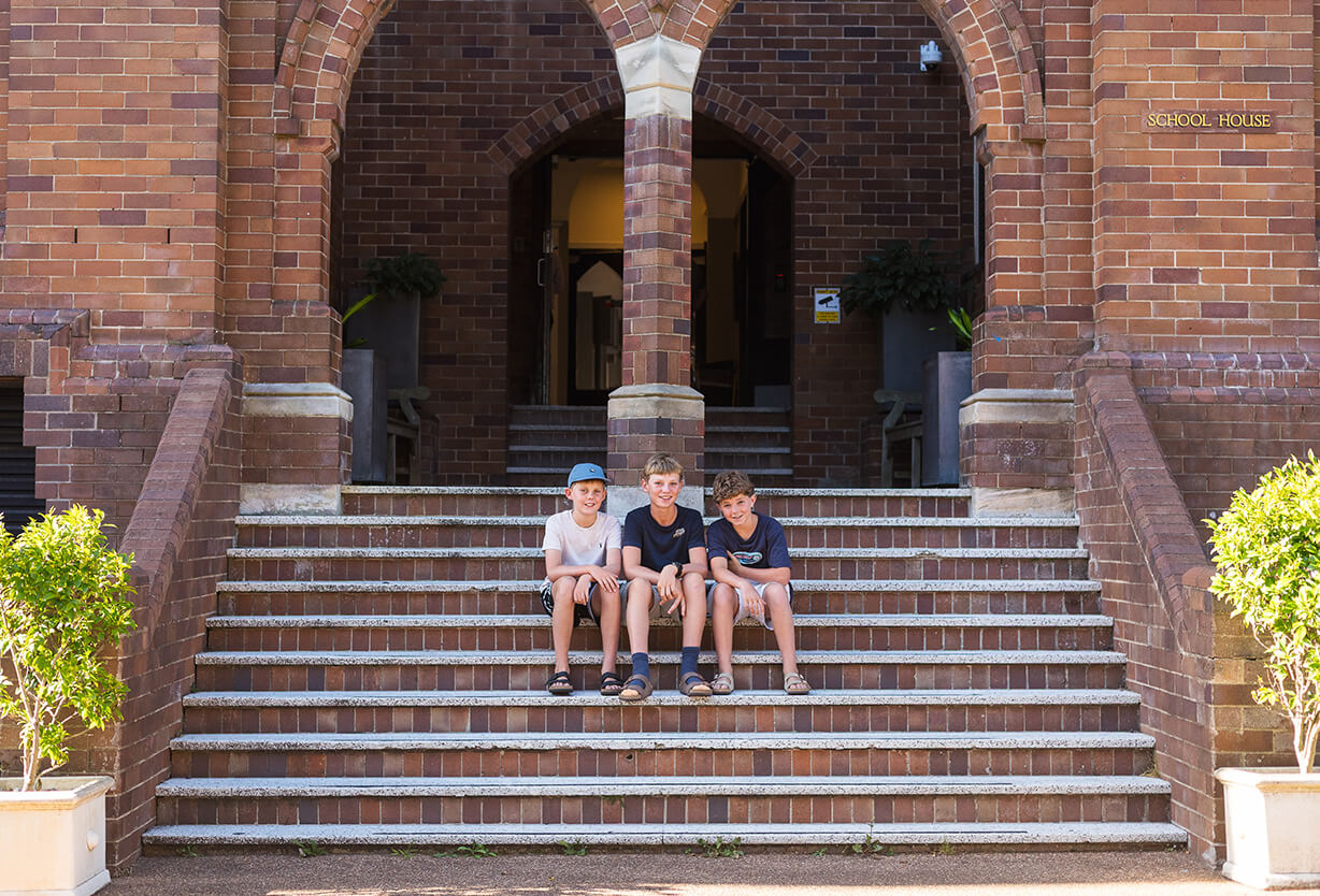 Three students sitting at the steps to the entrance of the boarding house